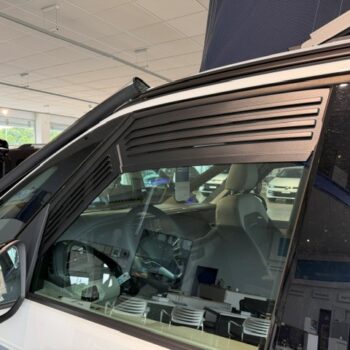 Close-up of a white van on display in a showroom; driver-side window and dashboard visible, with other vehicles in the background.